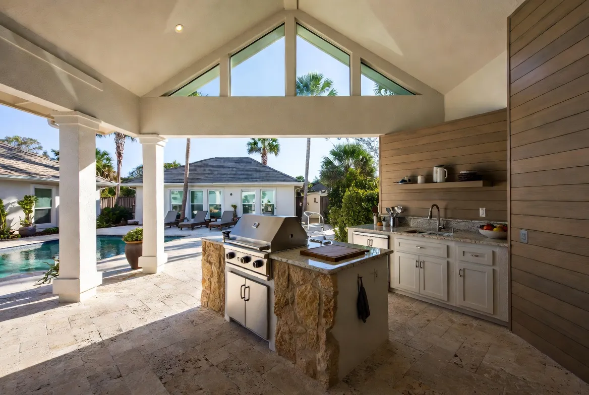 Poolside outdoor kitchen cabana with stone island grill on a travertine patio.