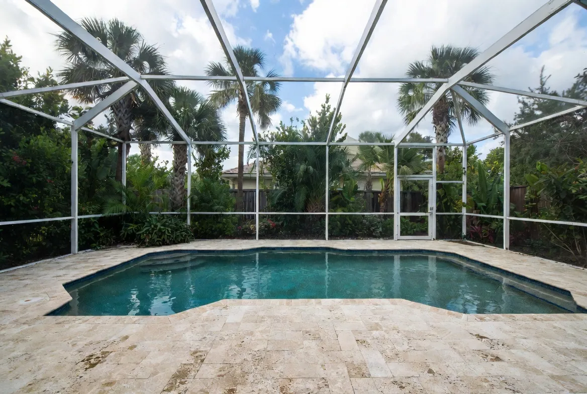 Screened pool enclosure (lanai) with a travertine deck and lush tropical landscaping in Southwest Florida.